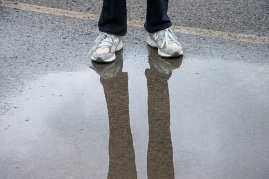 A person standing on a wet road, you can only see their shoes