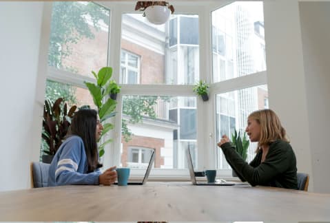 Two people meeting at a table with laptops in a casual setting