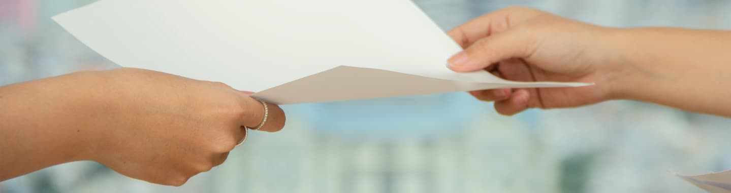 A hand handing a piece of paper to another